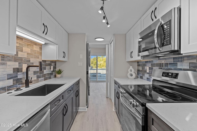 kitchen featuring white cabinets, appliances with stainless steel finishes, sink, light wood-type flooring, and light stone counters