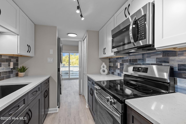 kitchen featuring light stone countertops, white cabinets, appliances with stainless steel finishes, backsplash, and light hardwood / wood-style flooring