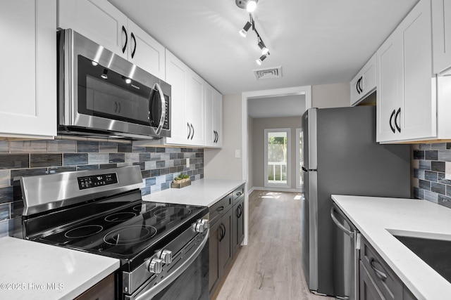 kitchen featuring appliances with stainless steel finishes, white cabinetry, decorative backsplash, rail lighting, and light wood-type flooring