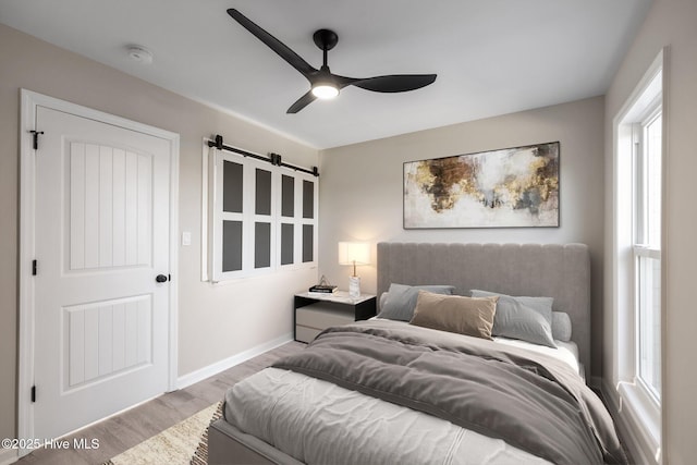 bedroom with light hardwood / wood-style flooring, ceiling fan, and a barn door