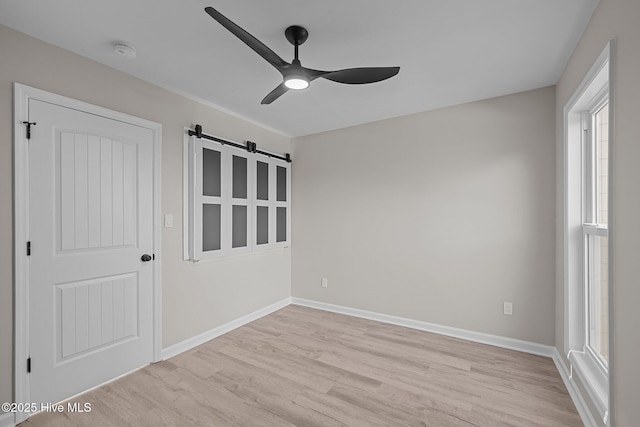 spare room with ceiling fan, light hardwood / wood-style flooring, and a barn door