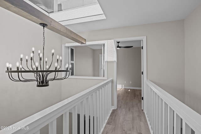 hall with light hardwood / wood-style flooring, beam ceiling, and an inviting chandelier