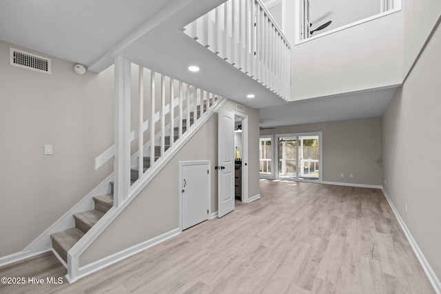 staircase with ceiling fan, a high ceiling, and wood-type flooring