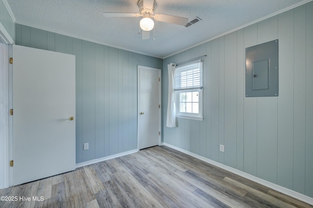 spare room with crown molding, electric panel, a textured ceiling, and light wood-type flooring