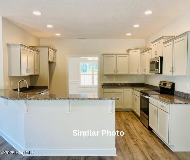 kitchen featuring a textured ceiling, appliances with stainless steel finishes, dark stone countertops, kitchen peninsula, and light hardwood / wood-style flooring