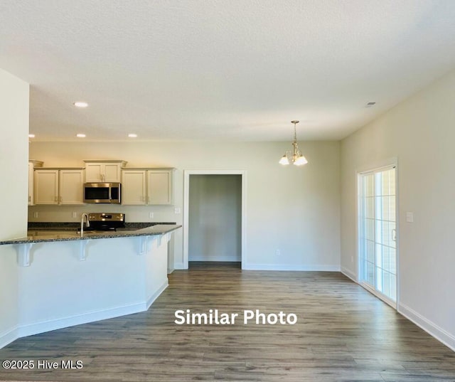 kitchen featuring pendant lighting, dark hardwood / wood-style flooring, a kitchen breakfast bar, stainless steel appliances, and dark stone counters