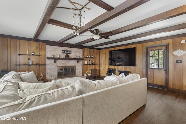 living room with dark hardwood / wood-style flooring, beamed ceiling, ceiling fan, wood walls, and a brick fireplace