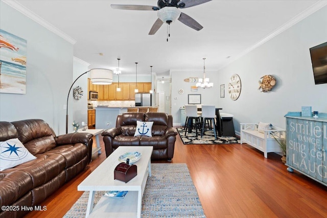 living room featuring ceiling fan with notable chandelier, ornamental molding, wood finished floors, and baseboards