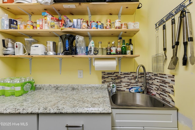 kitchen with light stone counters, sink, decorative backsplash, and white cabinets