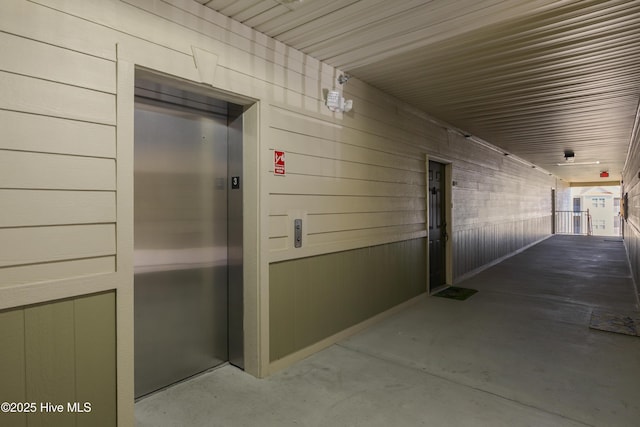 hall with wood walls, concrete floors, and elevator