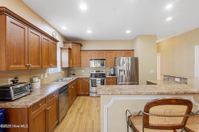 kitchen with a breakfast bar, sink, tasteful backsplash, light wood-type flooring, and appliances with stainless steel finishes