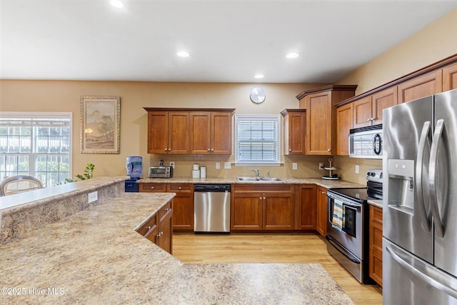 kitchen featuring sink, appliances with stainless steel finishes, tasteful backsplash, light stone counters, and light wood-type flooring