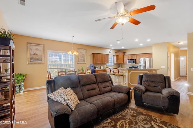 living room with ceiling fan with notable chandelier and light hardwood / wood-style floors