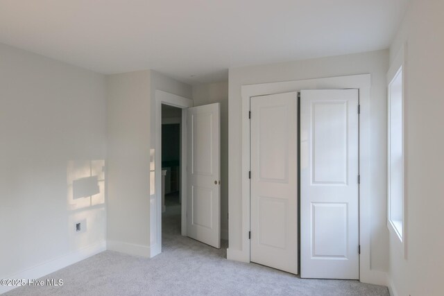 unfurnished bedroom featuring baseboards, a closet, and light colored carpet