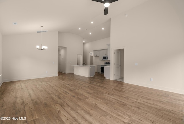 unfurnished living room featuring ceiling fan with notable chandelier, light hardwood / wood-style flooring, and high vaulted ceiling