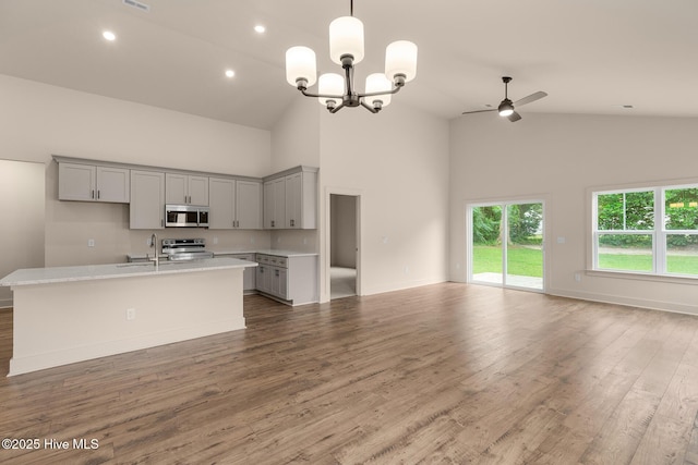 kitchen with ceiling fan with notable chandelier, appliances with stainless steel finishes, a center island with sink, and high vaulted ceiling