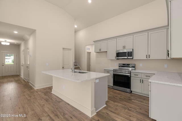 kitchen featuring lofted ceiling, sink, light stone countertops, an island with sink, and stainless steel appliances