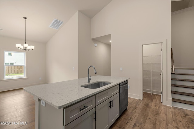 kitchen featuring stainless steel dishwasher, sink, hanging light fixtures, an island with sink, and light stone counters