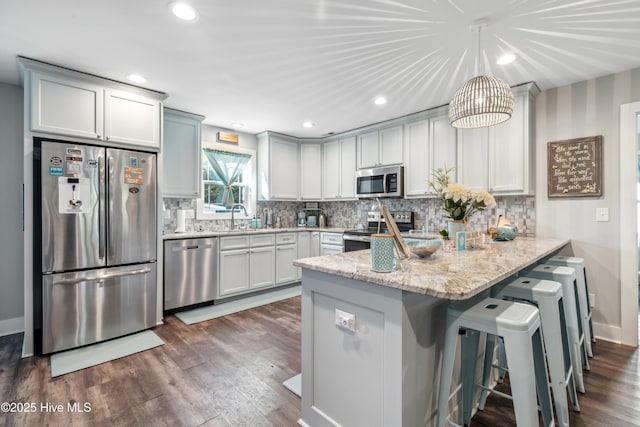 kitchen with sink, decorative light fixtures, kitchen peninsula, stainless steel appliances, and light stone countertops