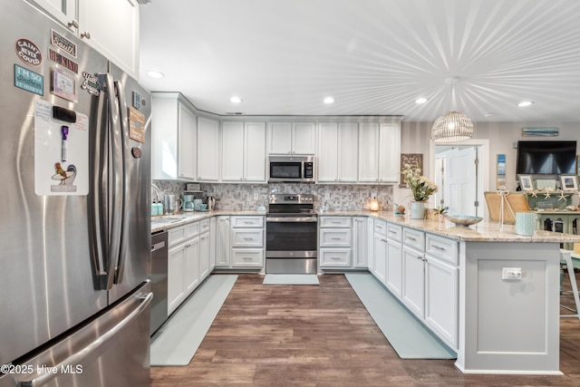 kitchen with appliances with stainless steel finishes, light stone countertops, hanging light fixtures, and white cabinets