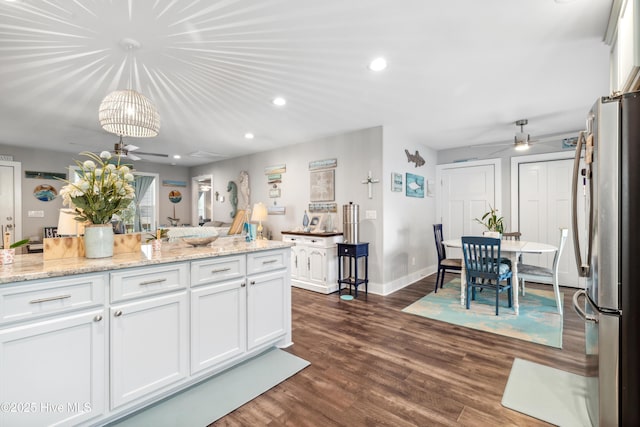 kitchen with stainless steel refrigerator, decorative light fixtures, white cabinets, light stone countertops, and dark wood-type flooring