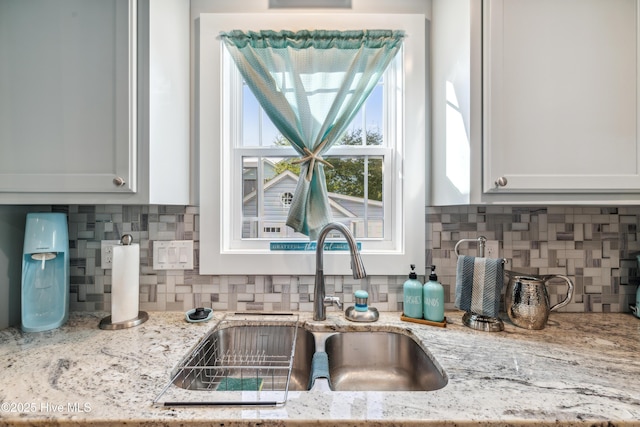 kitchen with light stone countertops, sink, white cabinets, and decorative backsplash