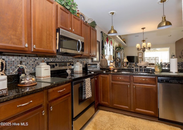 kitchen featuring pendant lighting, dark stone counters, decorative backsplash, appliances with stainless steel finishes, and brown cabinetry