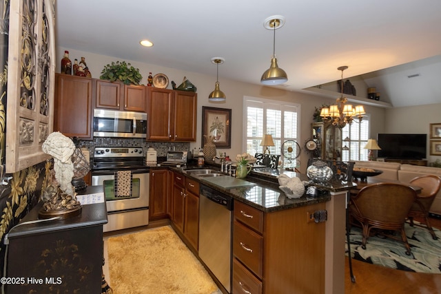 kitchen featuring brown cabinets, backsplash, appliances with stainless steel finishes, a peninsula, and a chandelier