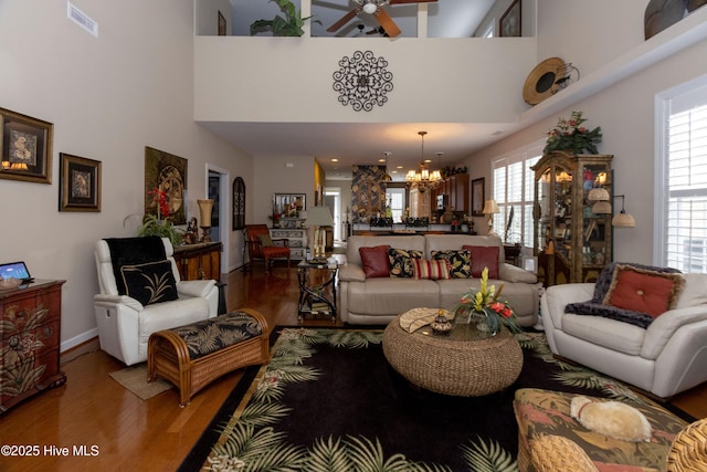 living room featuring baseboards, ceiling fan with notable chandelier, visible vents, and light wood-type flooring