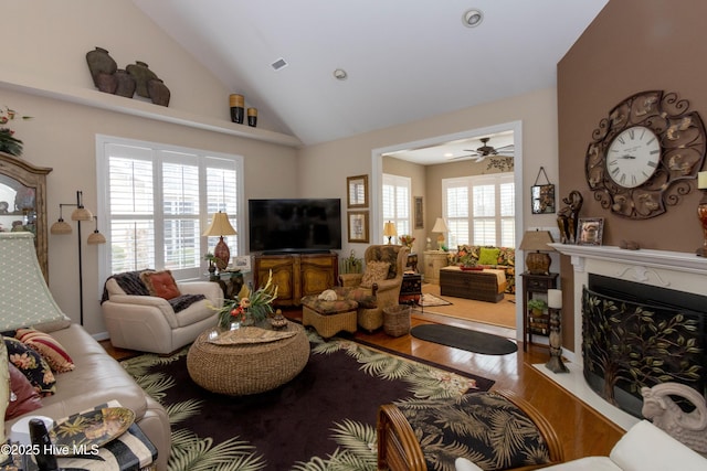 living area with a fireplace, high vaulted ceiling, wood finished floors, and ceiling fan