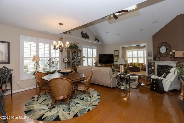 dining space with wood finished floors, visible vents, a fireplace, vaulted ceiling, and ceiling fan with notable chandelier