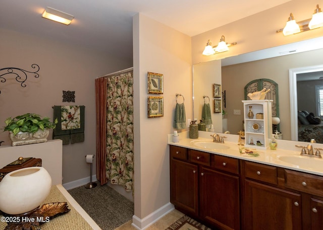 full bathroom with a sink, baseboards, double vanity, and tile patterned floors