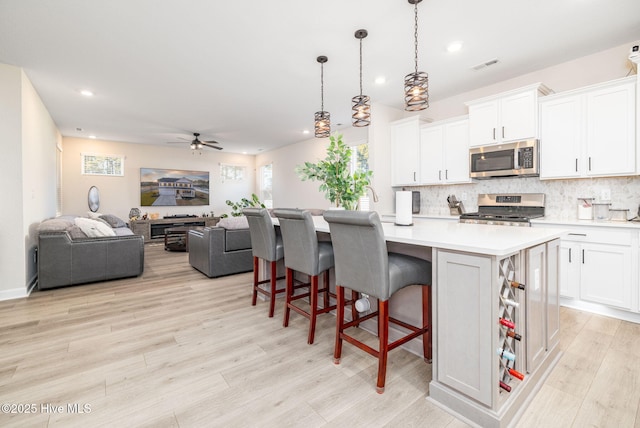 kitchen featuring a kitchen bar, white cabinetry, hanging light fixtures, a center island with sink, and stainless steel appliances