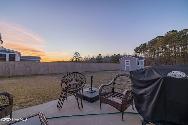 patio terrace at dusk featuring a grill, a yard, and a storage shed