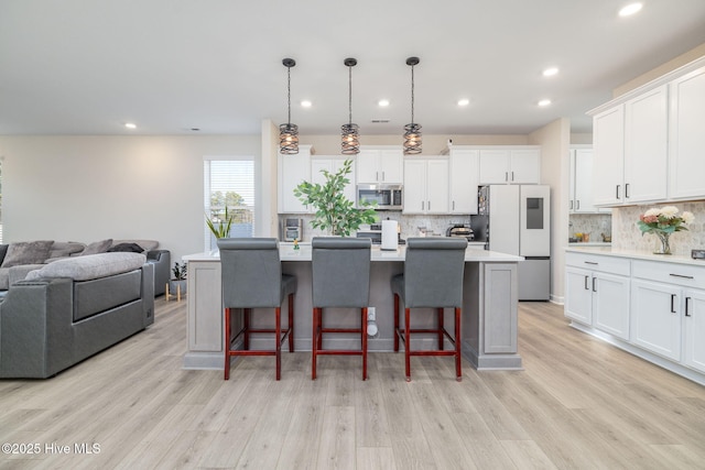 kitchen featuring appliances with stainless steel finishes, pendant lighting, white cabinetry, an island with sink, and a kitchen bar