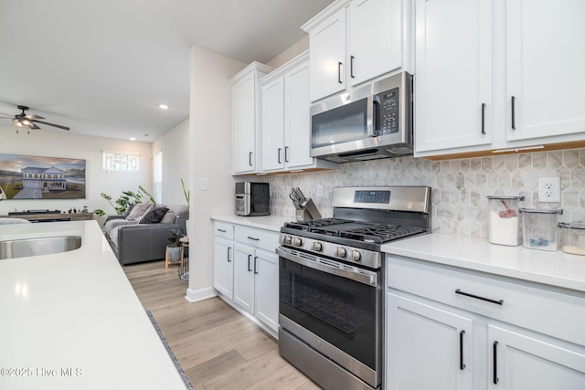 kitchen featuring light hardwood / wood-style flooring, white cabinets, ceiling fan, stainless steel appliances, and backsplash