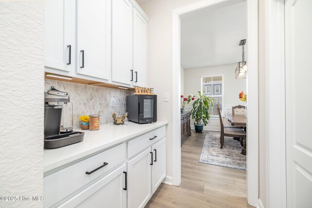 bar featuring white cabinetry, backsplash, decorative light fixtures, and light hardwood / wood-style flooring