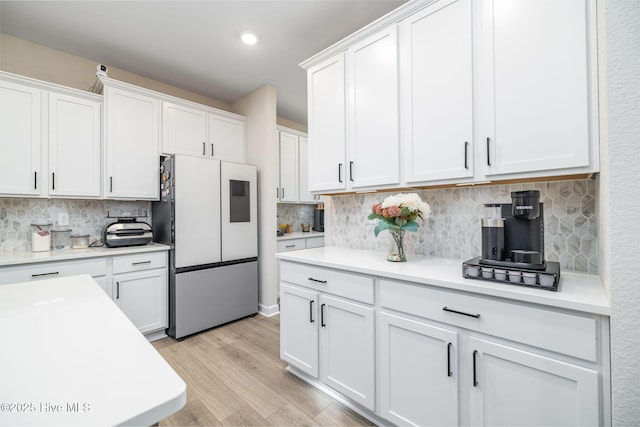 kitchen featuring white cabinetry, refrigerator, decorative backsplash, and light wood-type flooring