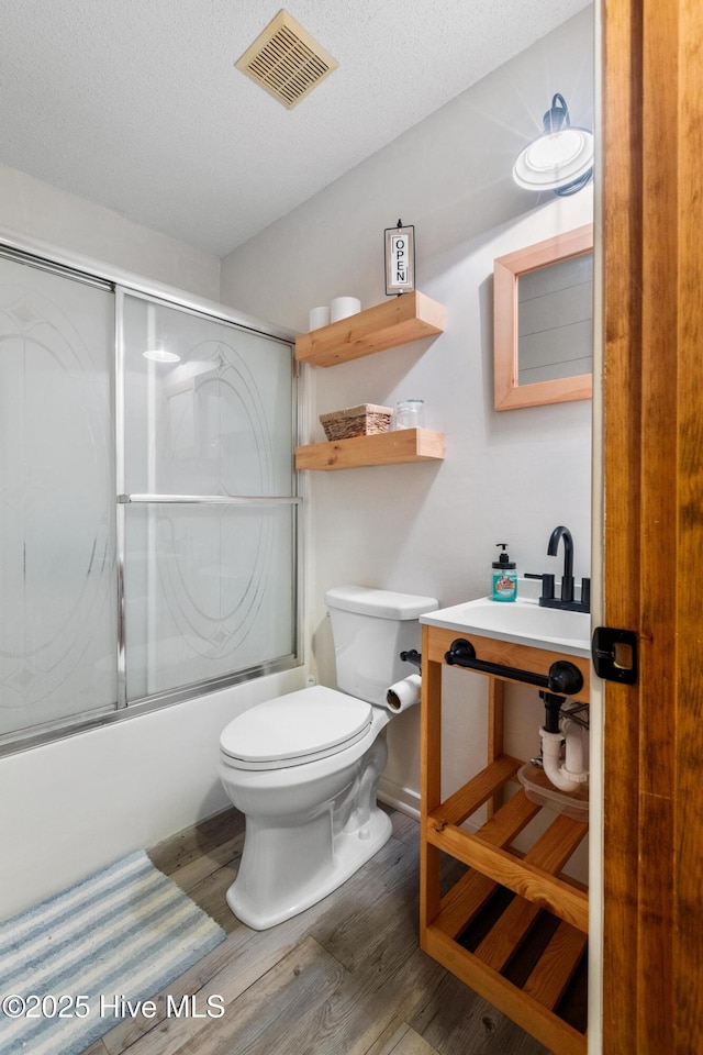 full bathroom with wood-type flooring, sink, toilet, a textured ceiling, and shower / bath combination with glass door