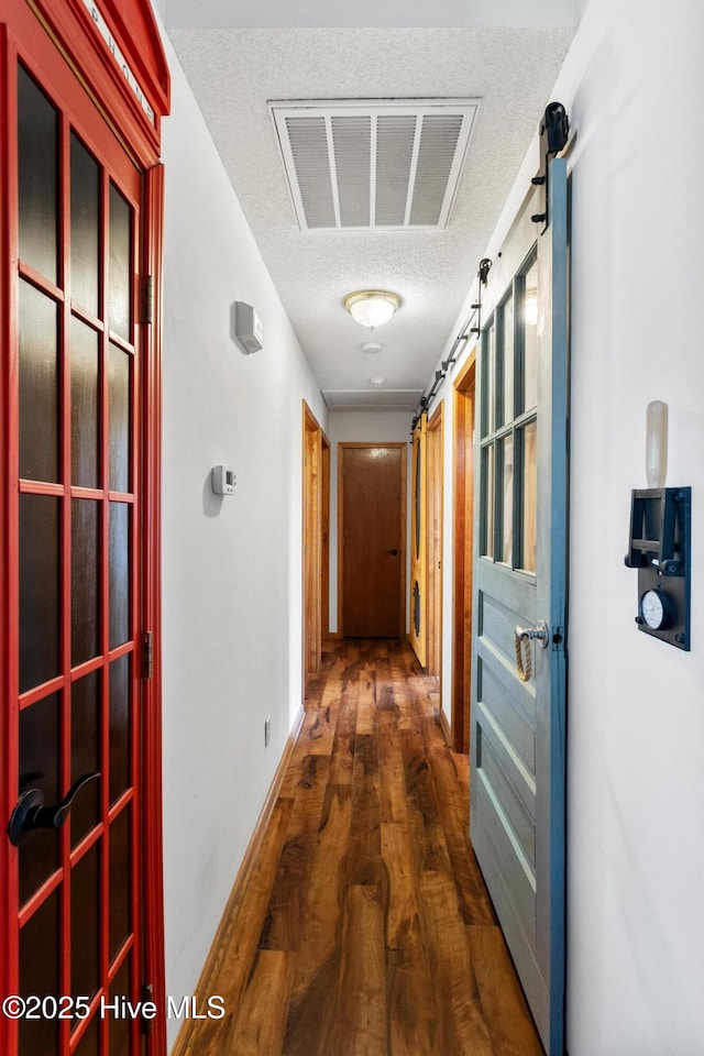 corridor with a barn door, dark hardwood / wood-style floors, and a textured ceiling