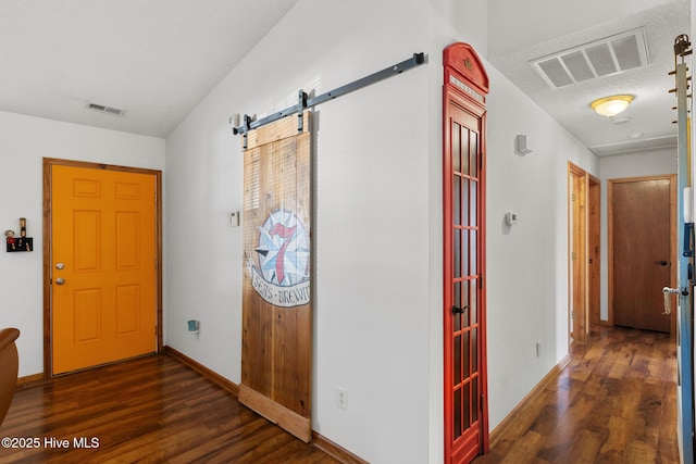 hallway with a barn door, a textured ceiling, and dark hardwood / wood-style flooring