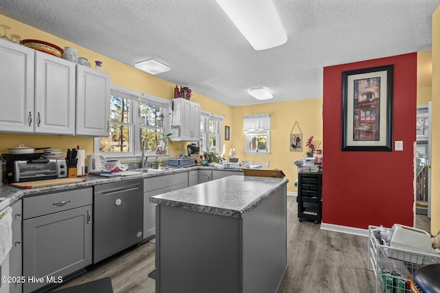 kitchen featuring light hardwood / wood-style floors, dishwasher, gray cabinetry, sink, and a kitchen island