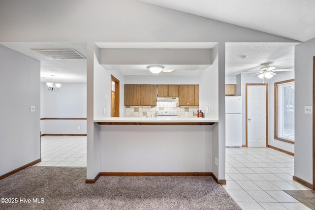 kitchen featuring lofted ceiling, decorative backsplash, white fridge, light tile patterned floors, and kitchen peninsula