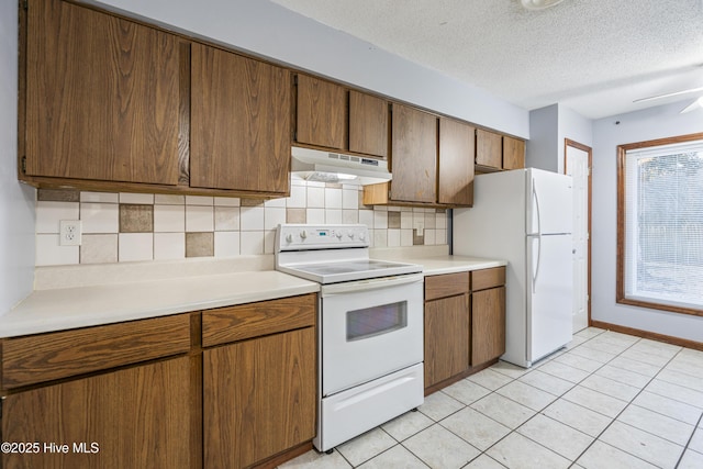 kitchen featuring decorative backsplash, white appliances, light tile patterned flooring, and a textured ceiling