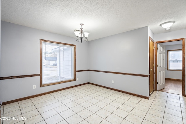 tiled spare room featuring a textured ceiling and a notable chandelier