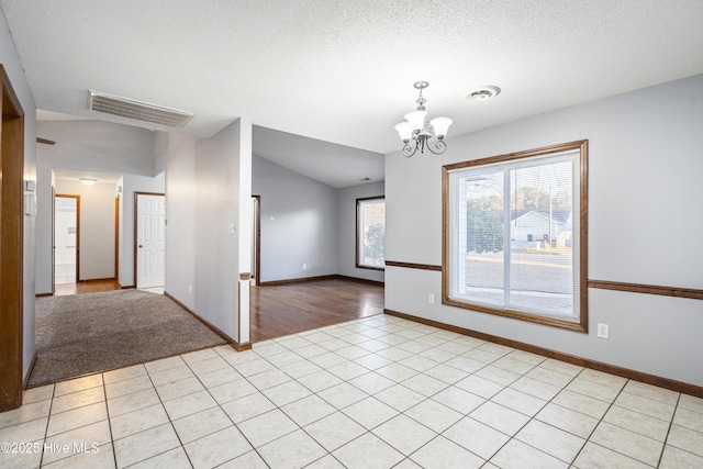 tiled empty room featuring an inviting chandelier, lofted ceiling, and a textured ceiling