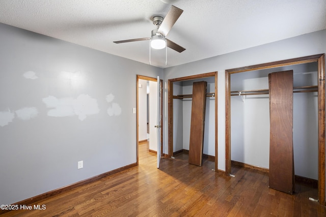 unfurnished bedroom featuring dark wood-type flooring, ceiling fan, a textured ceiling, and two closets