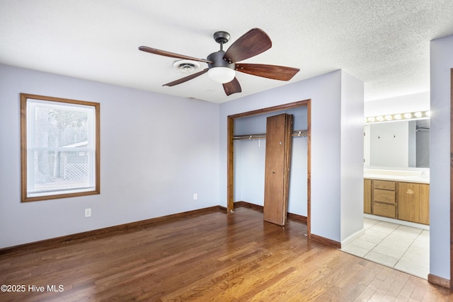 unfurnished bedroom with connected bathroom, a closet, ceiling fan, a textured ceiling, and light hardwood / wood-style flooring