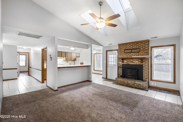 unfurnished living room with a wealth of natural light, light carpet, vaulted ceiling with skylight, and ceiling fan