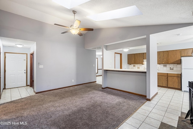 unfurnished living room with ceiling fan, vaulted ceiling with skylight, and light tile patterned floors